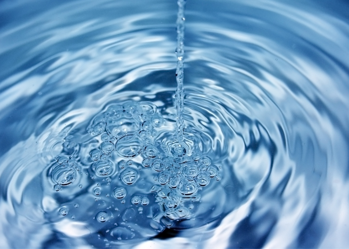 Stream of water creating bubbles and ripples on a clear surface.