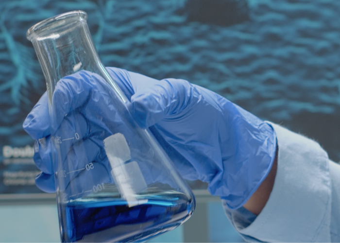Scientist in gloves analyzing blue liquid in a beaker in a laboratory.